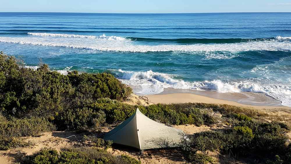 A tent in the dunes with the Tasman see in the background and blue skies