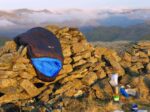 A black Criterion Quantum 450 sleeping bag is draped over a wall airing after a night wild camping in the Lake District. Hills and mist are in back ground
